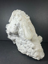 White stilbite crystals clustered on a rough, textured matrix, viewed against a dark gray background highlighting the mineral's natural formation.