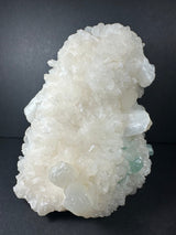 Translucent white stilbite crystals forming a clustered, rounded mass with subtle pale green apophyllite crystals visible near the base against a dark background.