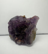 Cluster of purple cubic fluorite crystals displaying translucent and shiny surfaces with hints of brown and white mineral inclusions on a light background.
