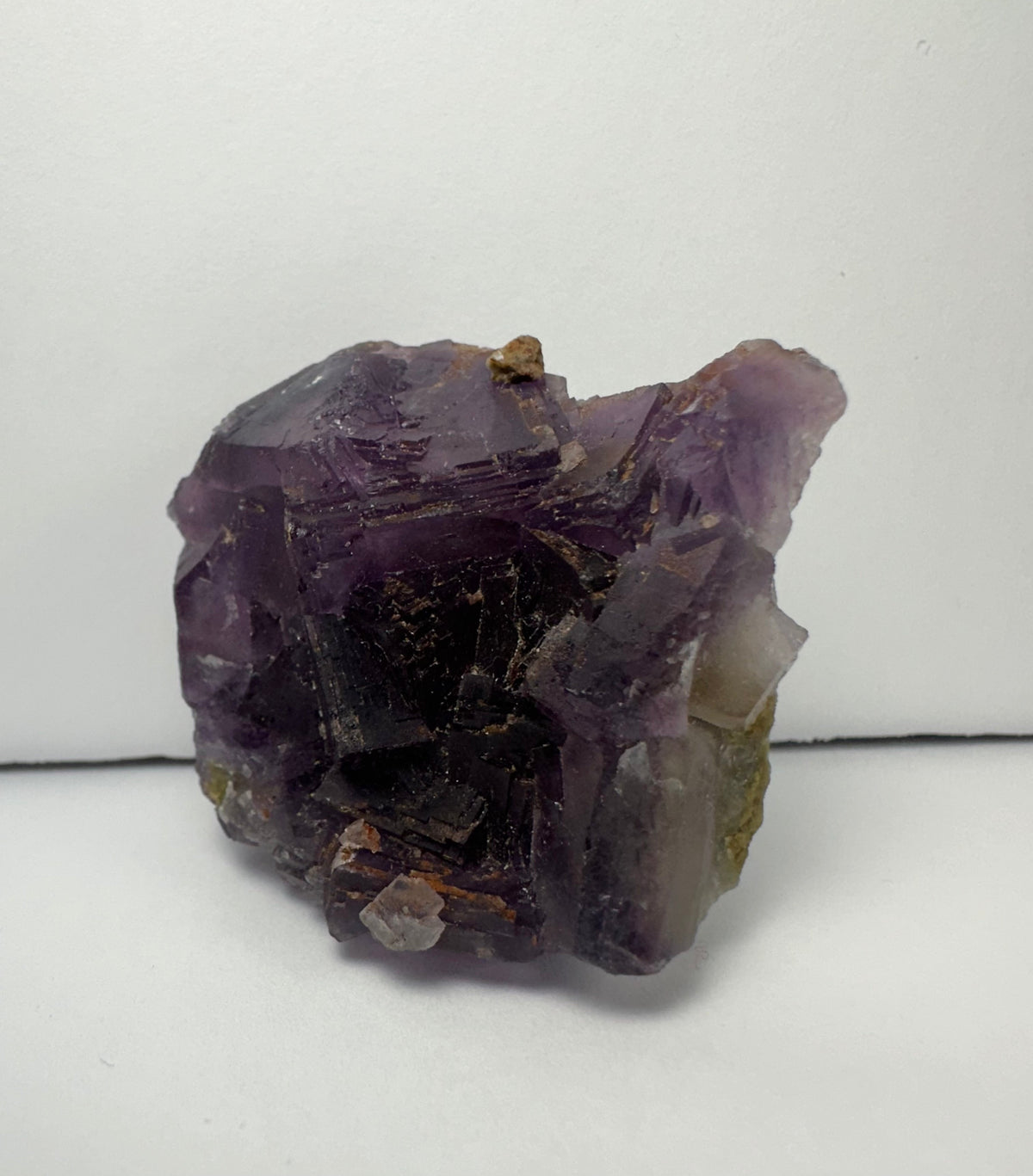 Cluster of purple cubic fluorite crystals displaying translucent and shiny surfaces with hints of brown and white mineral inclusions on a light background.