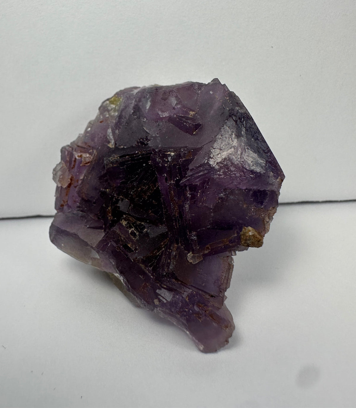 Purple cubic fluorite crystal cluster with translucent to opaque surfaces and sharp geometric edges, resting on a pale matrix against a plain white background.