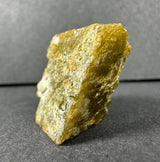 Rough yellow-brown siderite mineral sample with a textured, crystalline surface and angular shape, displayed upright against a gray background.