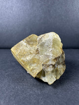 Yellow cubic fluorite cluster with translucent, glassy surfaces and natural crystalline structure, resting on a dark gray textured background.