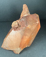 Tangerine quartz crystal cluster with distinct orange hues and textured mineral growths on a dark background.