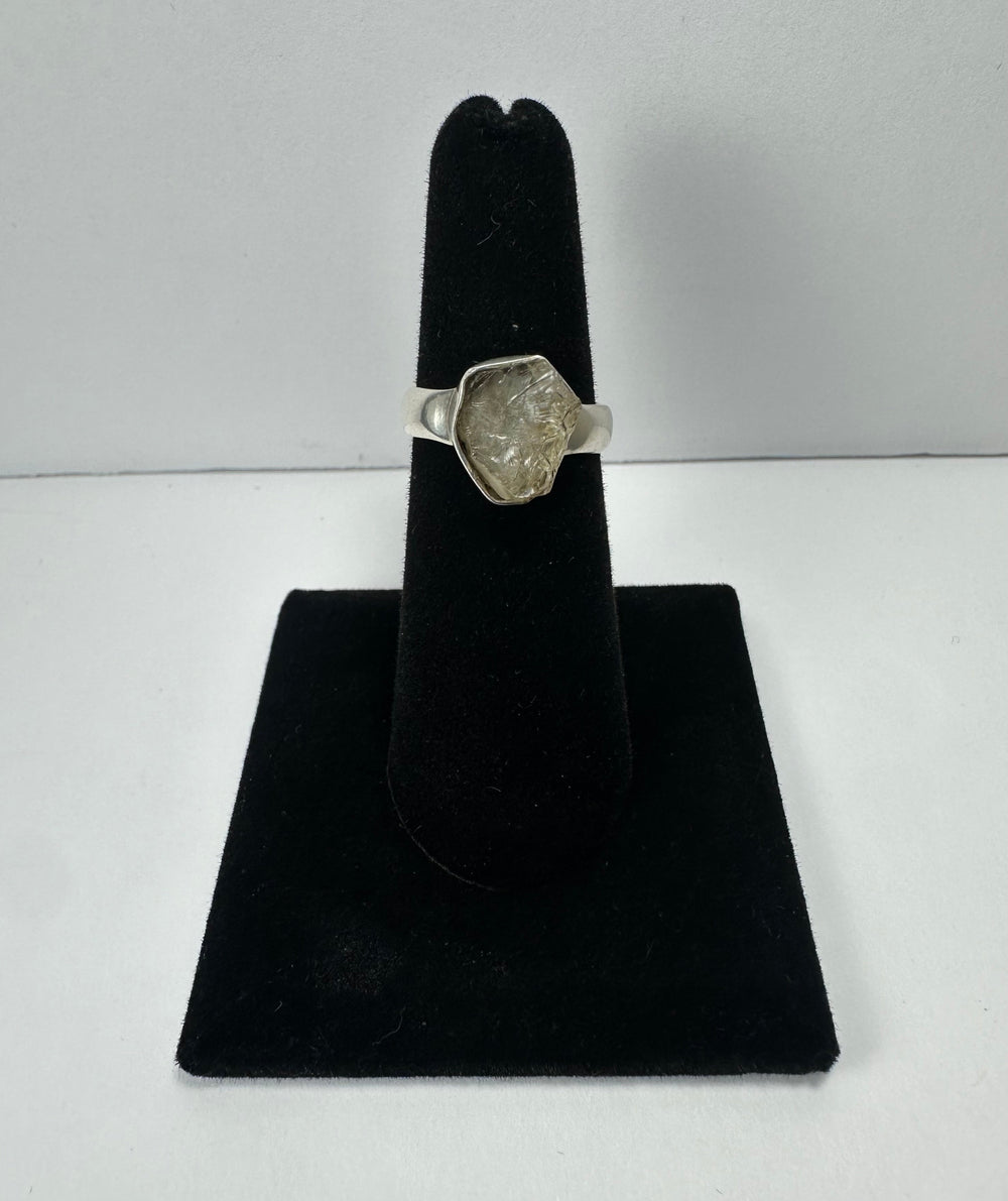 Silver ring with an irregularly shaped translucent quartz stone set in a simple band, displayed on a black velvet ring holder against a plain background.