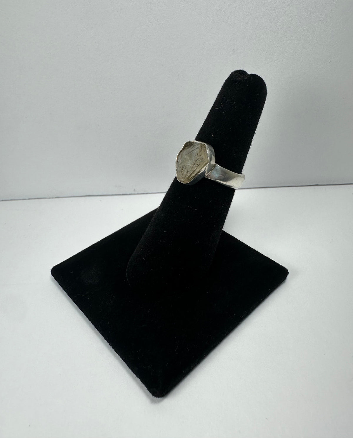 Silver ring with a polished quartz stone set in a hexagonal bezel, displayed on a black velvet ring holder against a plain white background.