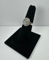 Round moonstone set in a silver bezel ring, displayed on a black velvet finger stand against a plain background.