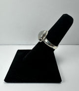 Silver ring with a polished round moonstone set in a bezel, displayed upright on a black velvet ring holder against a plain white background.