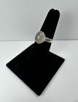 Silver ring with a polished round rose quartz cabochon set in a simple bezel, displayed on a black velvet ring holder against a white background.