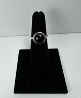 Silver ring with a polished black onyx stone set in a simple bezel, displayed on a black velvet stand against a plain white background.