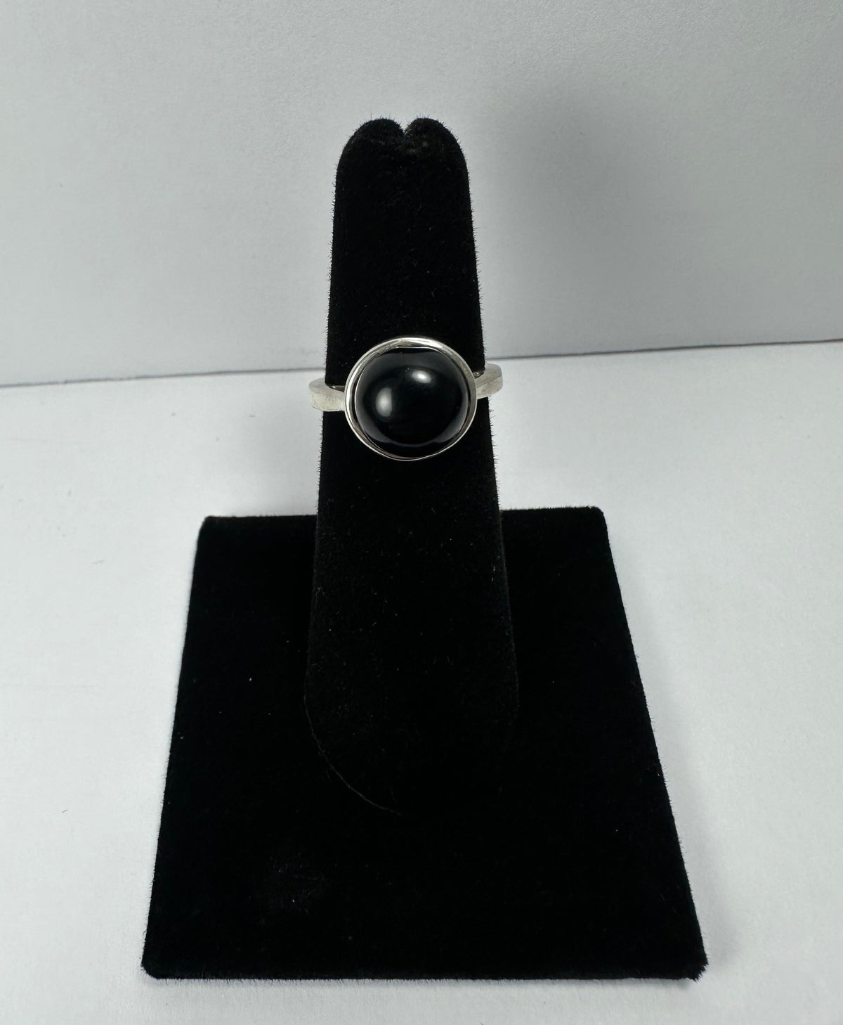 Silver ring with a polished black onyx stone set in a simple bezel, displayed on a black velvet stand against a plain white background.