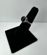 Silver ring with a polished round black onyx stone mounted on a black velvet ring display stand against a plain white background.
