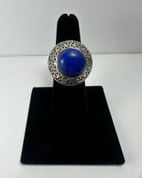 Silver ring with a large round deep blue lapis lazuli stone surrounded by intricate filigree detailing, displayed on a black velvet finger stand.