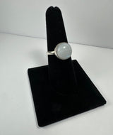 Round moonstone set in a silver bezel on a simple silver band, displayed on a black velvet ring holder against a white background.