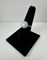 Round moonstone ring with a smooth, pale iridescent surface set on a simple silver band displayed on a vertical black velvet ring holder.