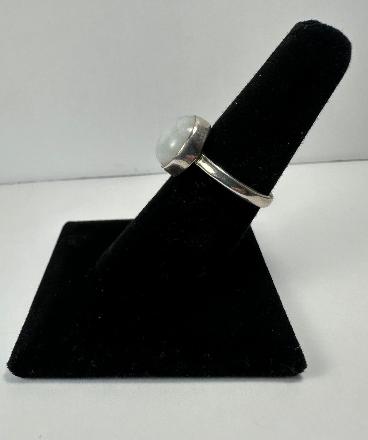 Silver ring with a round moonstone cabochon set in a simple bezel, displayed on a black velvet ring holder against a plain white background.