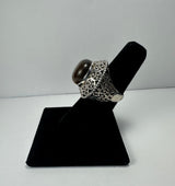 Silver ring with intricate circular filigree patterns featuring a polished dark tiger's eye stone set prominently on top, displayed on a black velvet stand.