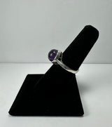Silver ring with a smooth round amethyst stone set in a simple bezel on a black velvet ring display.