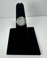 Round moonstone ring with a silver bezel setting displayed upright on a black velvet ring holder against a plain white background.