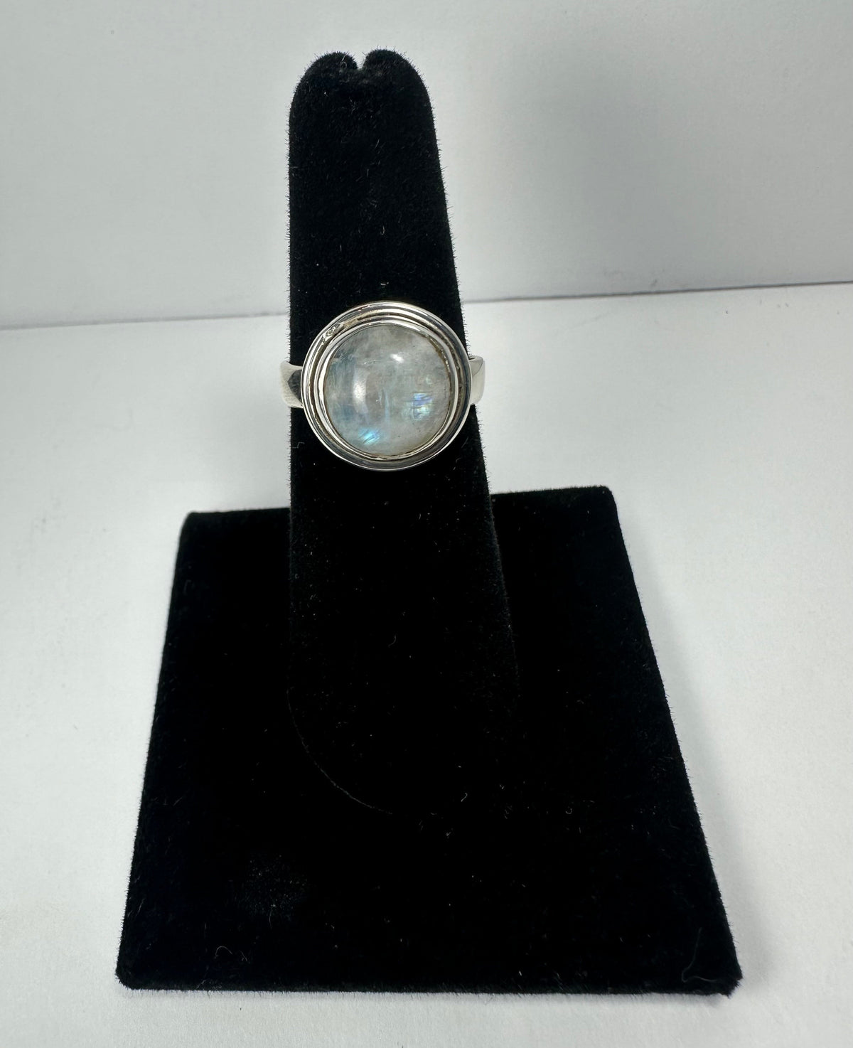 Round moonstone ring with a silver bezel setting displayed upright on a black velvet ring holder against a plain white background.