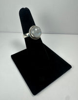Silver ring featuring a round moonstone with a pale blue iridescence, set in a smooth bezel on a narrow band, displayed on a black velvet ring holder.