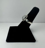 Silver ring with a round cabochon moonstone centered atop a smooth silver band, displayed on a black velvet ring holder against a plain light background.