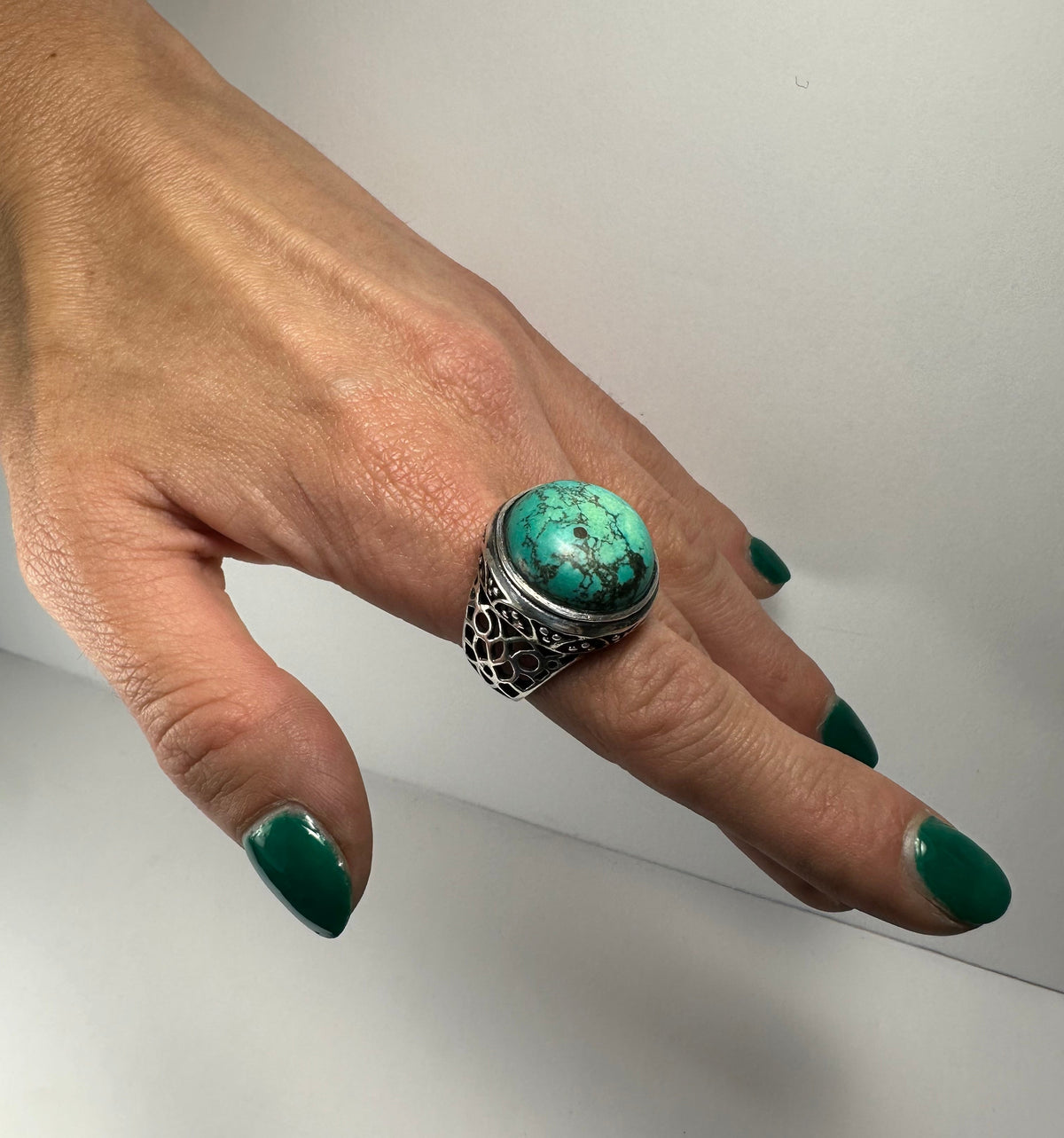 Hand wearing an ornate silver ring with a large oval turquoise stone featuring black veining, set against a plain white background.