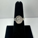 Silver ring with a smooth oval rose quartz stone set on a black velvet ring holder, shown against a plain light background.