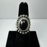 Silver ring with a polished oval dark red garnet center stone, surrounded by a beaded silver border, displayed on a black velvet stand.