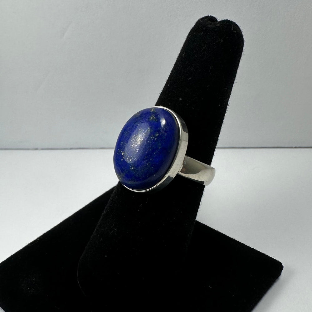 Silver ring with an oval lapis lazuli stone featuring deep blue shades and small gold flecks, displayed on a black velvet finger stand against a plain background.