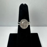 Silver ring with a smooth, oval rose quartz stone set in a simple bezel, displayed on a black velvet ring holder against a plain light background.