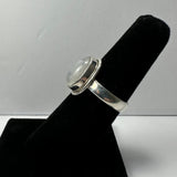 Silver ring with a smooth moonstone cabochon set in a rounded bezel, displayed on a black velvet finger stand against a plain light background.