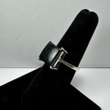 Silver ring with a square black onyx stone set in four prongs, displayed on a black velvet ring holder against a plain white background.