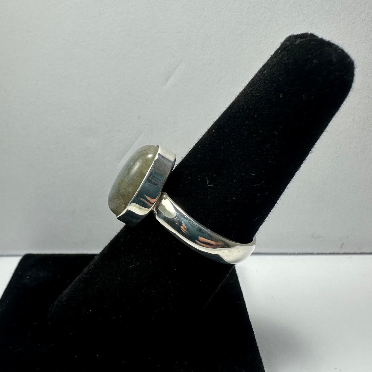 Silver ring with a polished labradorite stone set in a bezel, displayed on a black ring holder against a plain white background.