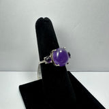 Silver ring with a central polished round amethyst and two smaller amethyst stones on either side, displayed on a black velvet ring holder.