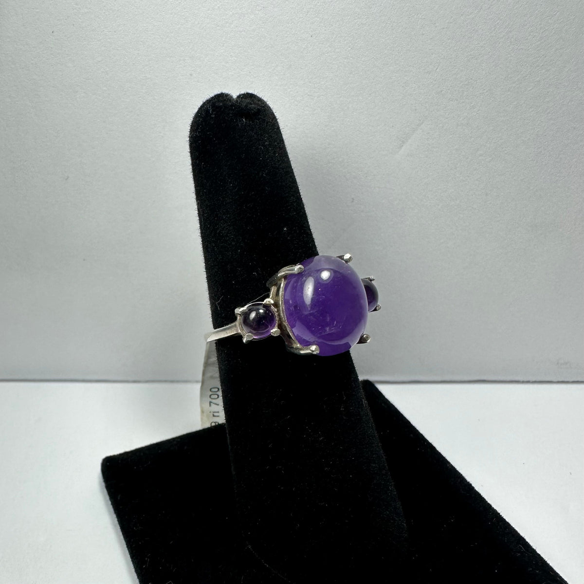 Silver ring with a central polished round amethyst and two smaller amethyst stones on either side, displayed on a black velvet ring holder.