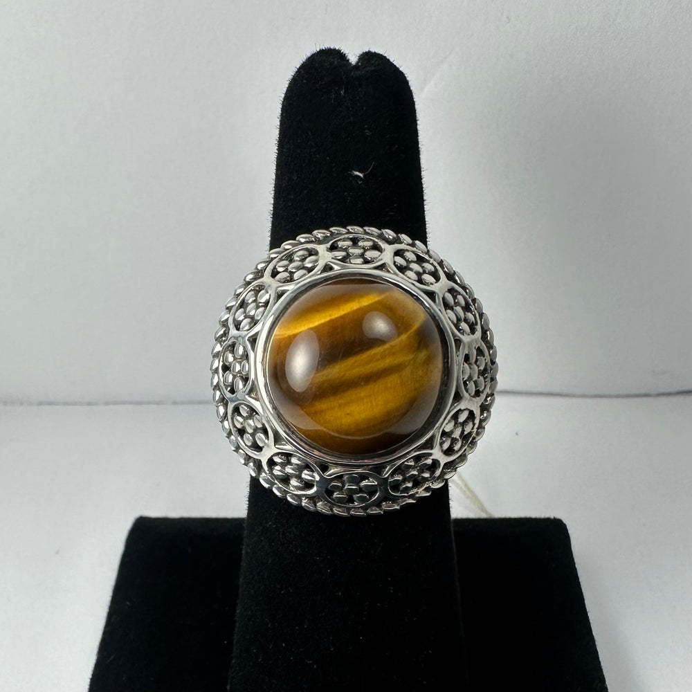 Round tiger's eye stone with brown and golden stripes set in detailed silver filigree band on black velvet ring display.