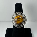 Round tiger's eye stone with brown and golden stripes set in detailed silver filigree band on black velvet ring display.