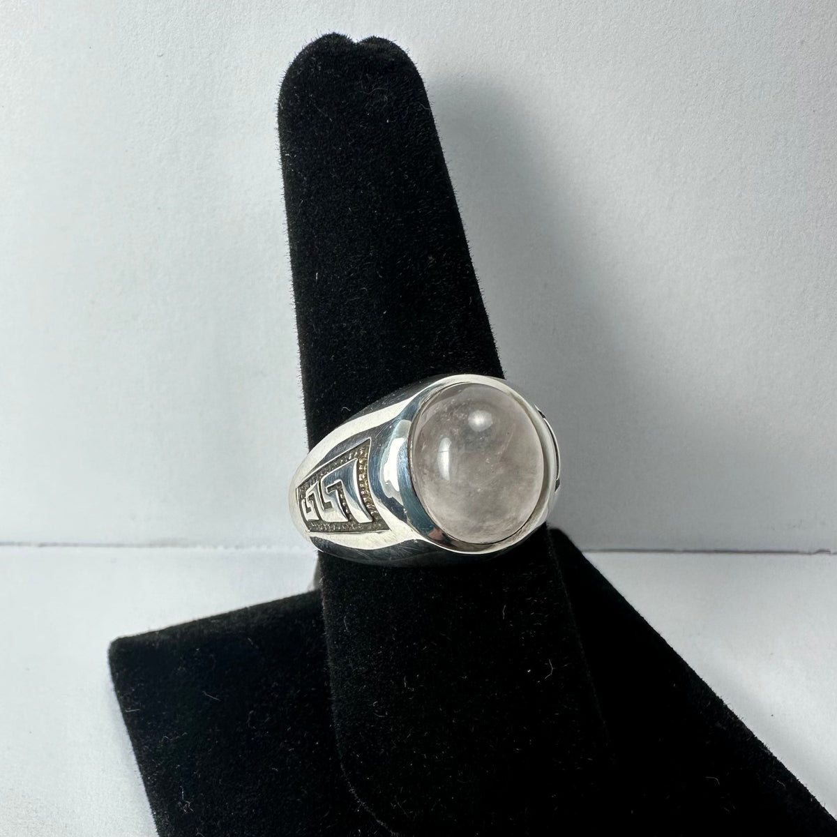Silver ring with a smooth, translucent moonstone cabochon set in a polished bezel, featuring a black geometric pattern on the band, displayed on a black velvet holder.
