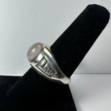 Silver ring with a smooth round translucent moonstone atop and geometric patterns on the band, displayed on a black velvet ring holder against a white background.