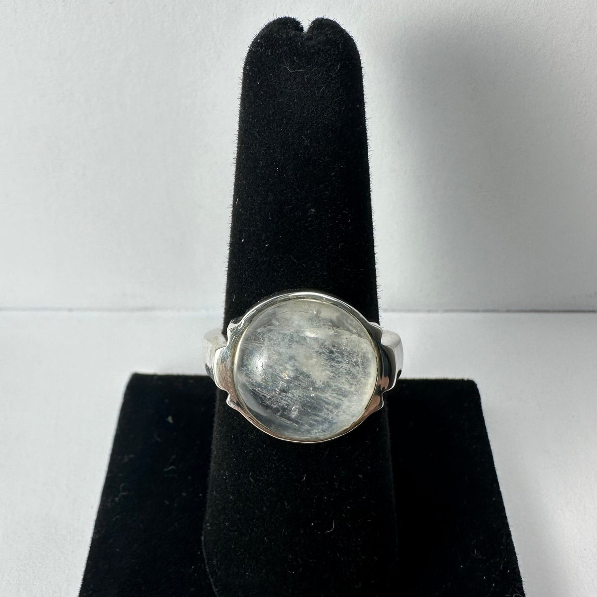 Silver ring with a polished translucent moonstone cabochon mounted in a smooth bezel setting, displayed on a black velvet ring stand.