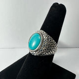 Silver ring with raised hexagonal pattern band and a smooth, oval turquoise stone set at the center, displayed on black velvet stand.