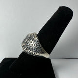Silver ring with a patterned band featuring geometric shapes and a smooth rose quartz stone set at the top, displayed on a black velvet finger stand.