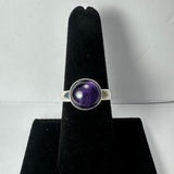 Silver ring with a round, polished amethyst stone set in a smooth bezel on a black velvet ring holder.