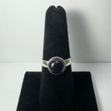 Silver ring with a round purple amethyst cabochon set in a bezel, displayed upright on a black velvet ring holder against a white background.