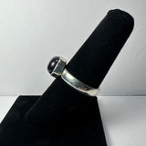 Silver ring with a round dark cabochon gemstone mounted on top, displayed on a black velvet ring holder against a white background.
