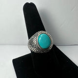 Silver ring with a textured hexagonal pattern band featuring a smooth, oval turquoise stone centerpiece, displayed upright on a black velvet finger stand.