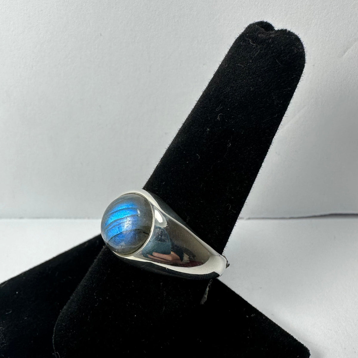 Silver ring with a rounded labradorite stone displaying blue iridescence, shown on a black velvet ring holder against a white background.