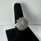 Silver ring with an ornate flower design featuring twisted rope-like petals, displayed on a black velvet finger stand against a plain white background.