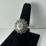 Silver ring with an intricate flower design featuring looped petals and a beaded center, displayed on a black velvet finger stand.